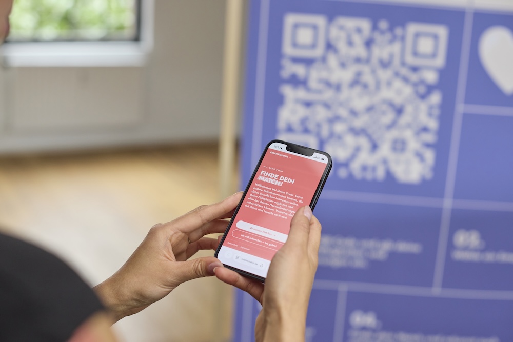 Teilnehmer:in mit der Creative-Match-Webapp auf dem Smartphone